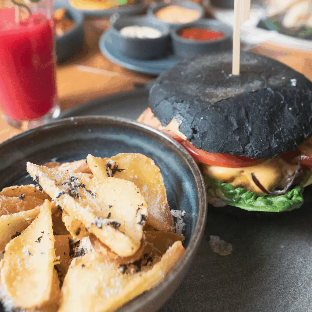 Burger mit schwarzem Brötchen, Kartoffelspalten und rotem Drink