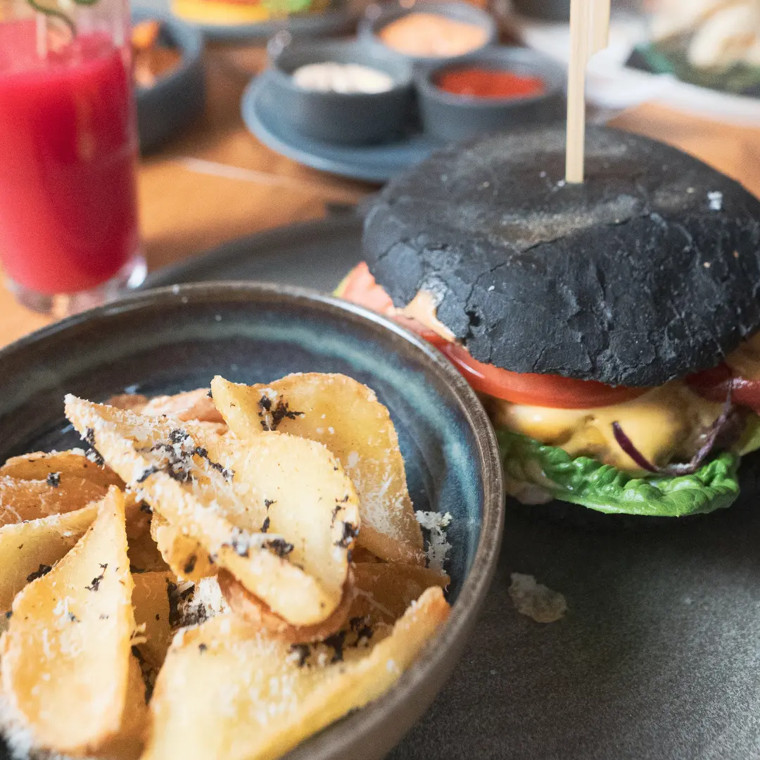 Burger mit schwarzem Brötchen, Kartoffelspalten und rotem Drink