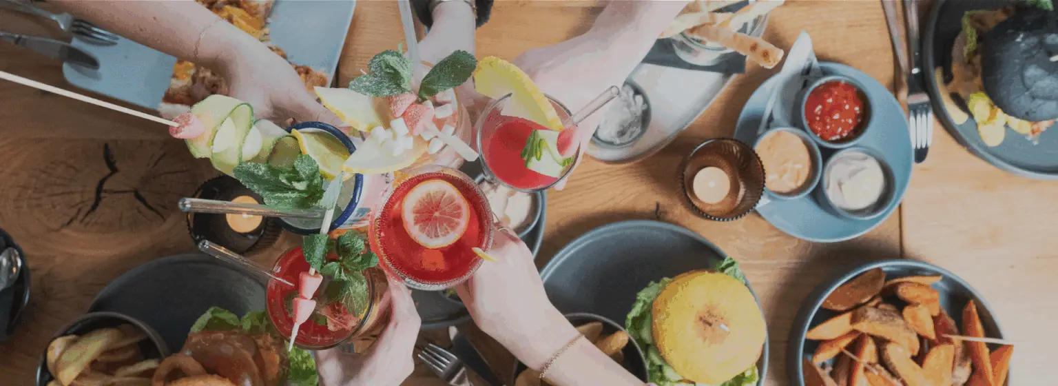 Freunde stoßen über einem gedeckten Tisch mit Drinks an
